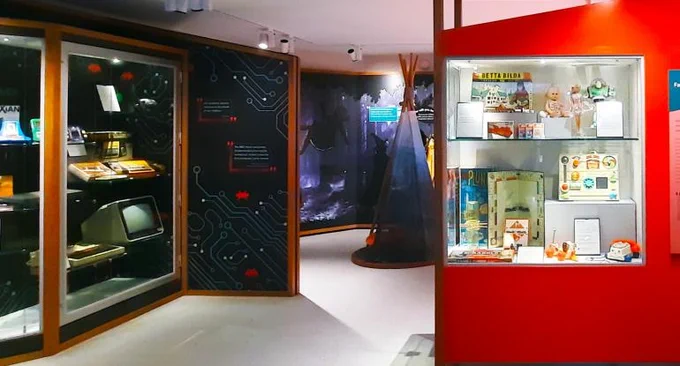 Photo of Gallery One in Museum of Childhood in Edinburgh. Display cases with objects and a tent in the middle of the floor. 