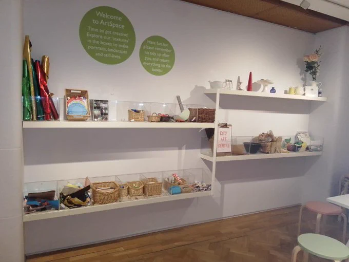 Photo of an art area in a gallery. Lots of perspex boxes hold art materials.