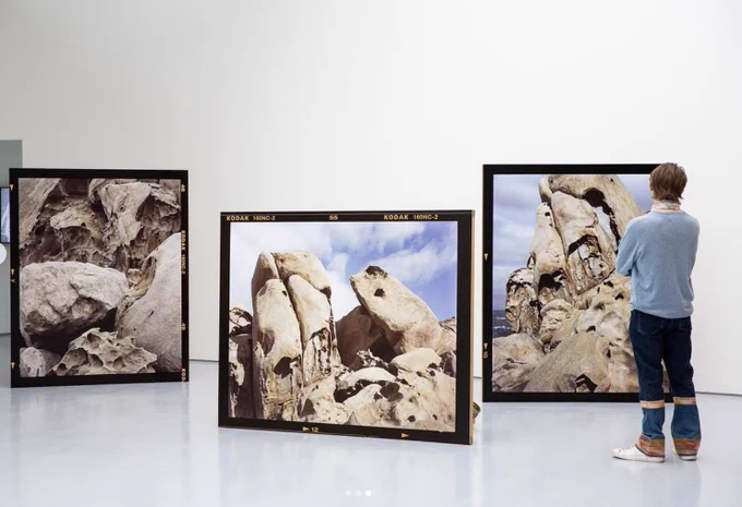 An installation shot of DCA's galleries with three large freestanding photographs of rock formations. A figure in blue stands looking at them to the right.