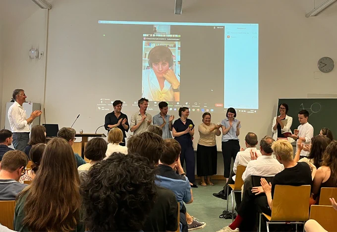 Teilnehmer:innen des Humanities Slam stehen klatschend vor dem Publikum.
