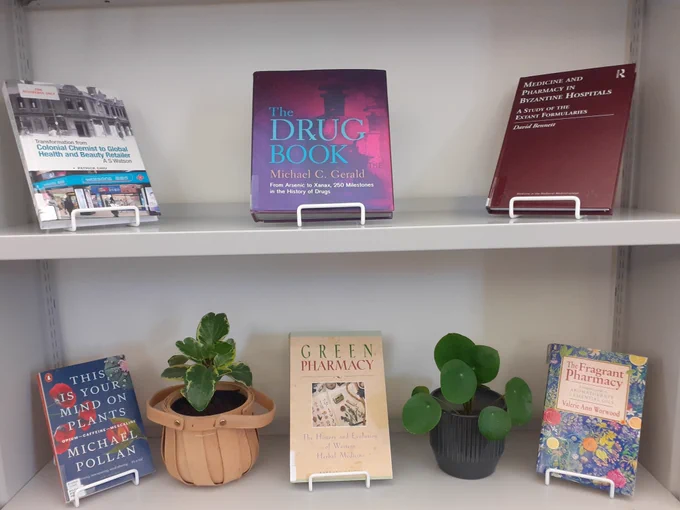 Selection of new books at the SOP Library. Six volumes and two small plants arranged on two metal shelves.