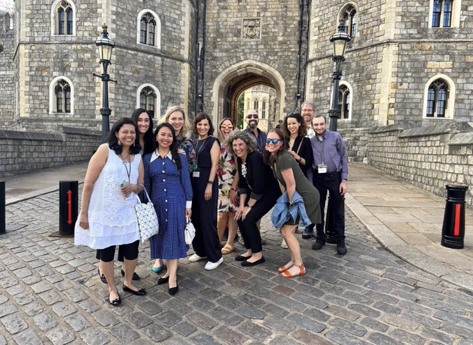 Group of men and women standing in front of Windsor Castle in Windsor, UK smiling.