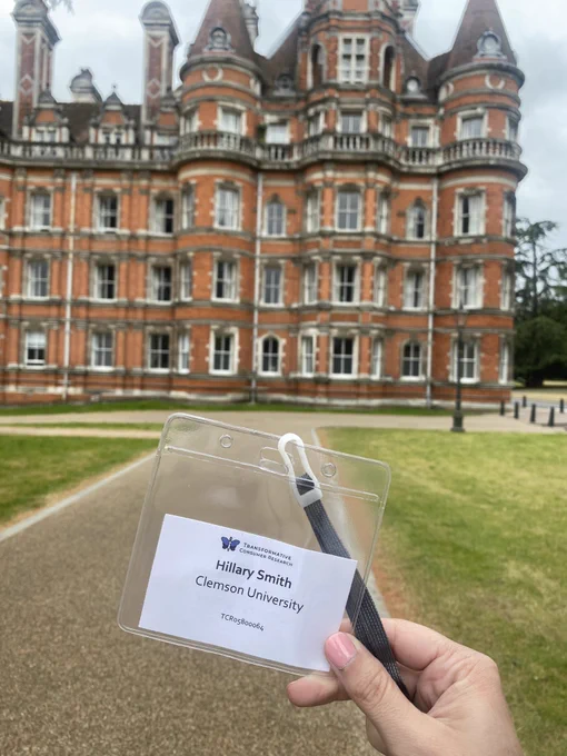 Badge from the Transformative Consumer Research conference held up in front of the byline at Royal Holloway. The badge says Hillary Smith Clemson University.