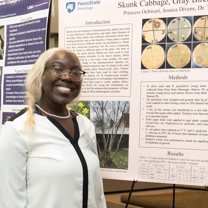 EnvironMentors program high school participant Princess Ochweri poses in front of a poster presentation for her research project.