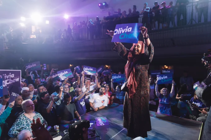 A woman holds a sign that reads ‘Olivia Chow for Mayor’ while dancing on stage.