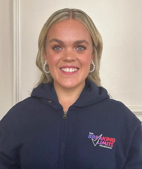 Ellie Simmonds is pictured smiling into the camera with pearl hoops and a navy hoodie that says 'Sure Breaking Limits programme' with the Sure tick going through the text 
