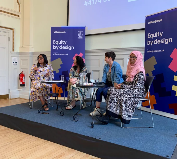 Three panelist’s and chair on the stage, in front of banners saying ‘equity by design’
