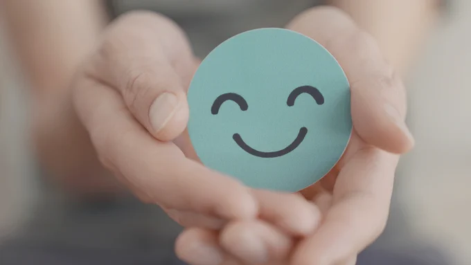 The image shows a turquise face being held in a hand. The face is smiling.
