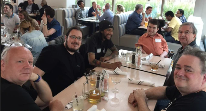 6 men of various ethnicities, one is in a wheelchair in a restuarant. 