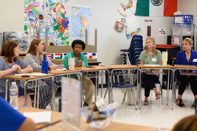 five people sitting at desks in a classroom talking to each other