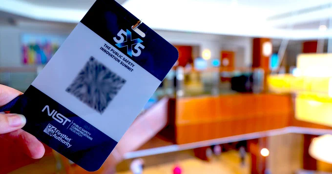 A person holding a 5x5 Summit badge inside a building;