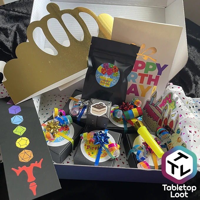 A box filled with colorfully wrapped boxes, bags, stickers, a card, a gold foil paper crown, a noise maker, and stickers.