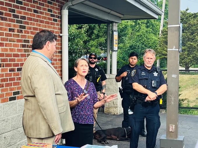 Rep. Michelle Mussman offering remarks while standing next to Mayor Rod Craig outside while police officers listen in the background.