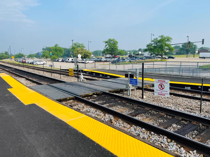 A view of the pedestrian crossing with yellow markings across railroad tracks on a sunny day.