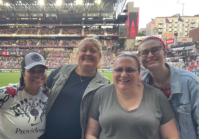 four employees posing for camera at providence park stadium during portland thorns washington spirit soccer game