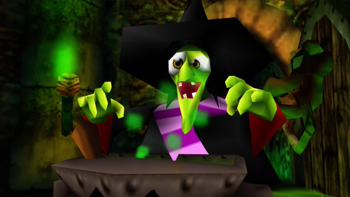 A green witch in a black hat and coat, and a purple and pink scarf, wiggles her fingers over a large pot.