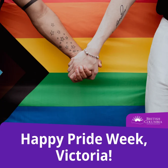 Text reads: Happy Pride Week, Victoria! 
Photo of two people holding hands in front of the progress Pride flag