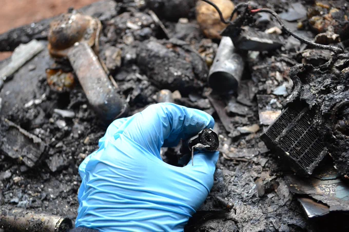 A fire investigator wearing gloves picks up a fragment from the fire.