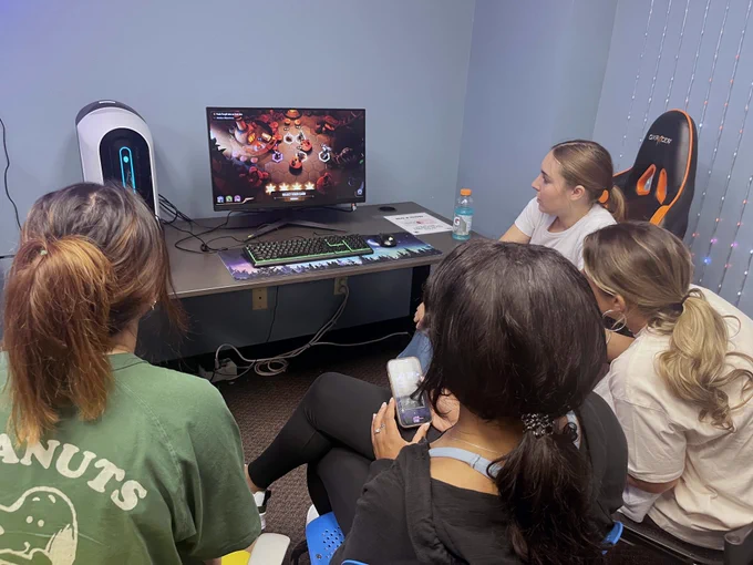[ID: Pictured is a photo of students playing a video game for a class at the UTA Central Library.]