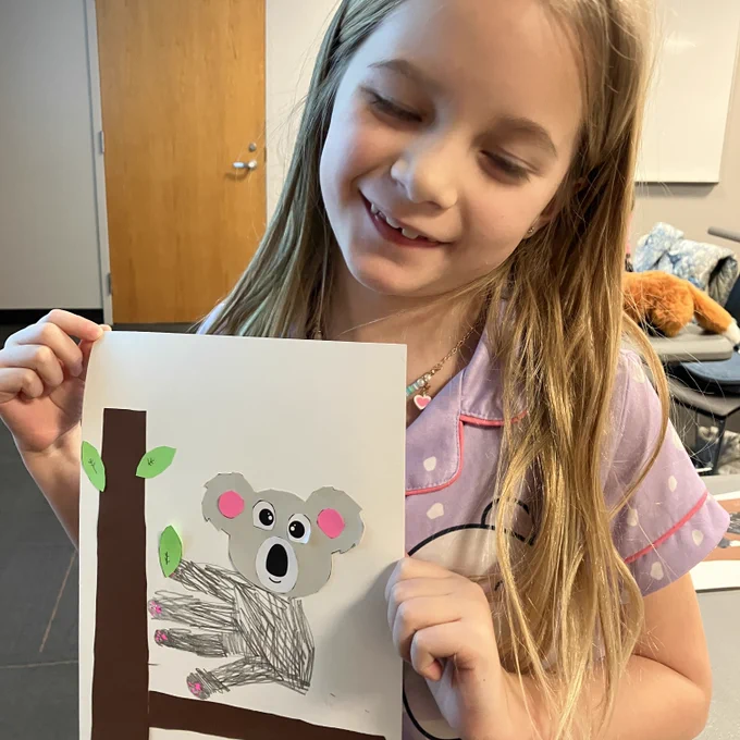 A young patrons holds up her koala artwork.