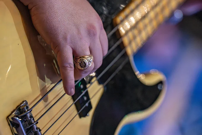 A hand with an Aggie ring on a finger strums a guitar. 