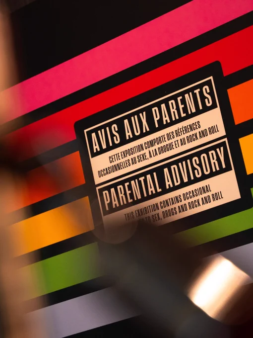 Parental Advisory label with French and English warnings about occasional sex, drugs, and rock and roll, displayed against a colorful striped background.