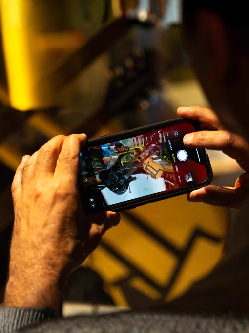 Personne prenant une photo d'une exposition colorée avec des guitars au Musée, à l'aide d'un téléphone intelligent.