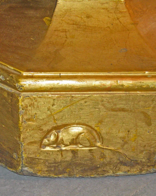 A close-up photograph of the base of a candlestick, carved with the small figure of a mouse
