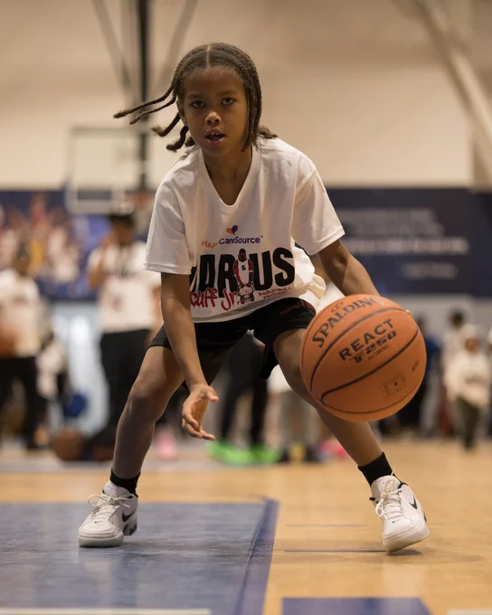 A young player dribbles a basketball intently on an indoor basketball court.