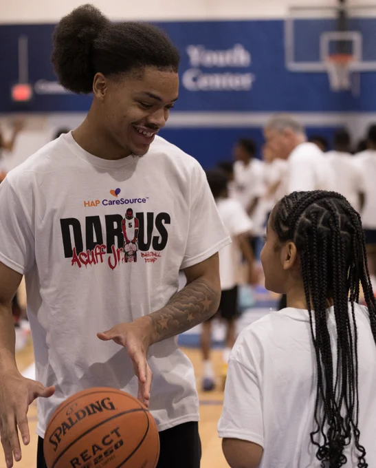 Two people interacting with each other while holding a basketball, one person is wearing a shirt with the HAP CareSource logo.