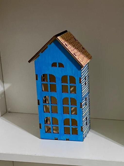 A little wooden house on a shelf with blue painted walls and a red-orange roof.