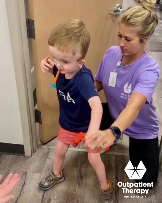 Physical therapist provides hands-on support as a child practices walking and coordination during an outpatient physical therapy session.