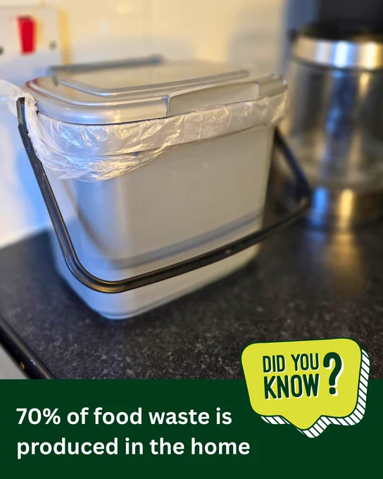 A silver food waste caddy with a black handle and lined with a clear plastic liner is next to a kettle on a kitchen worktop. Did you know? 70% of food waste is produced in the home.