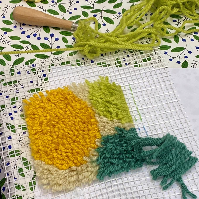 A tiled piece with yellow and green yarns punch through the holes.