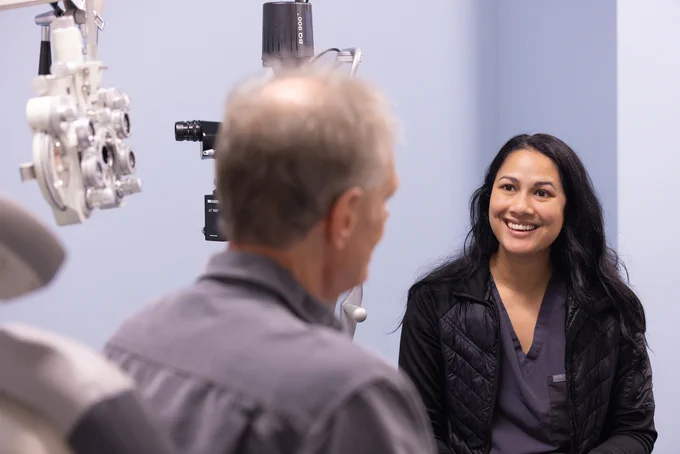 An ophthalmologist in a clinic is smiling at a patient seated at an eye examination machine.