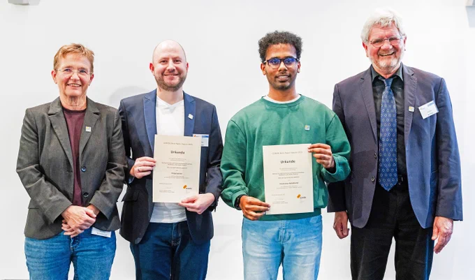 Four persons standing next to each other, two of them are holding a certificate.