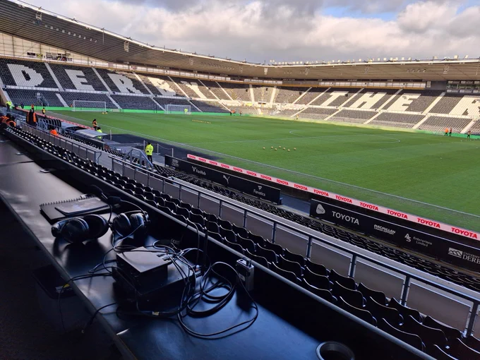A landscape photo taken from the end of the media table in the west stand. In the foreground is the setup our commentary team had for the day, we have the pitch in the background and then even further in the background than that is the north stand, north east corner and half of the east stand swallowed in sunshine!