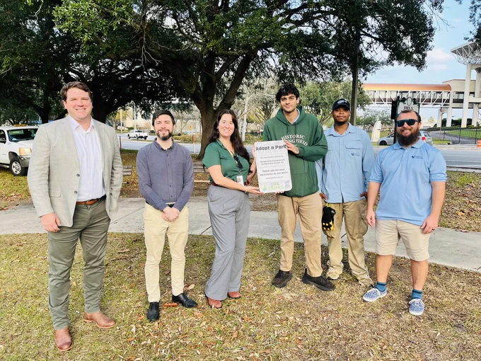 A group of people from SPAR and our parks department holding up a sign that says adopt a park on it