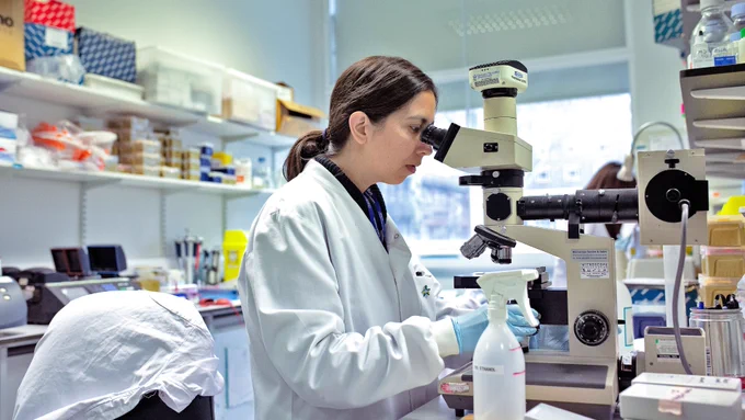 A scientist is working intently with a microscope in a laboratory environment, surrounded by various scientific equipment.