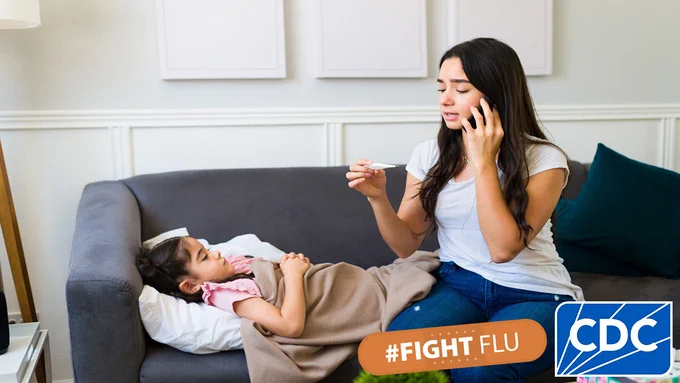 A sick child lays on the couch next to her mother. Her mother is looking at a thermometer while talking on the phone. #FightFlu and CDC branded logos are in the bottom right corner of the image. 