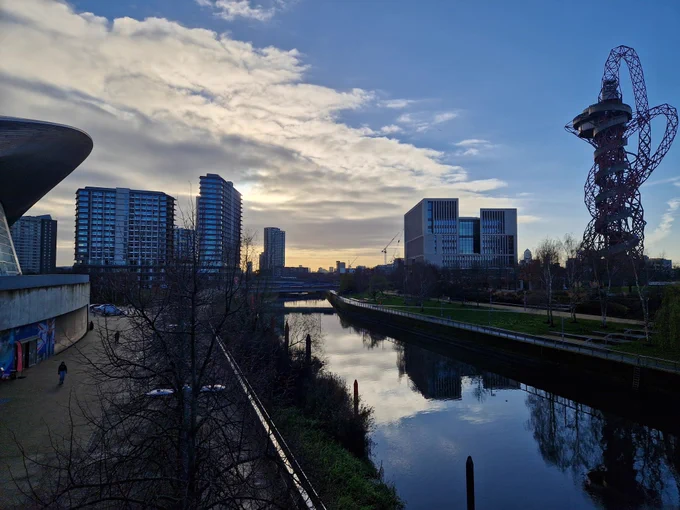 Image of morning sun over Queen Elizabeth Olympic Park - with blue sky, and imposing buildings riverside.