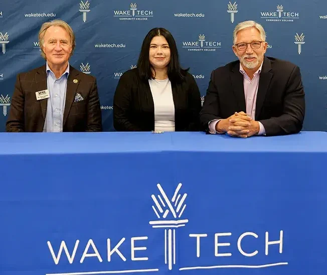 Three individuals standing behind a podium with a "Wake Tech" logo on the front at a Wake Tech Community College event.