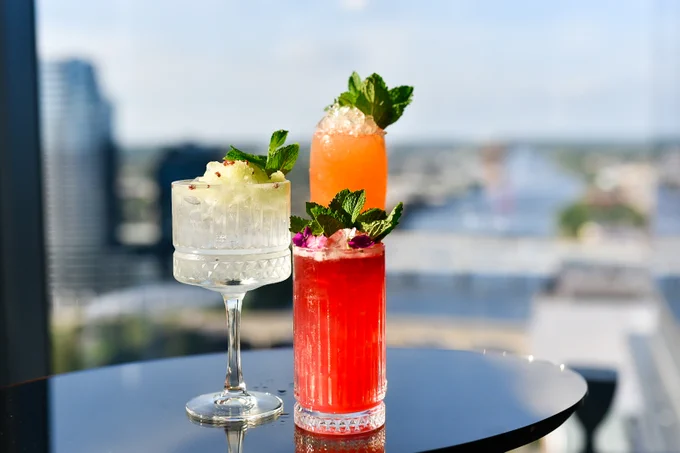Three mocktails on a rooftop bar with a cityscape in the background. 