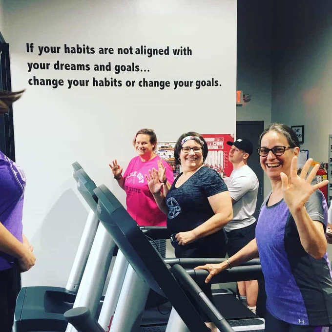 three smiling women walking on treadmills in a gym