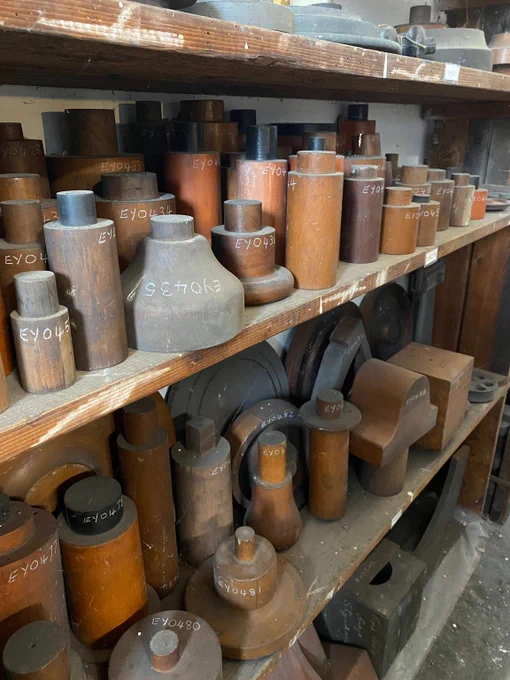 A collection of wooden patterns of various shapes and sizes, with white codes handwritten on them. They fill three shelves top to bottom. 