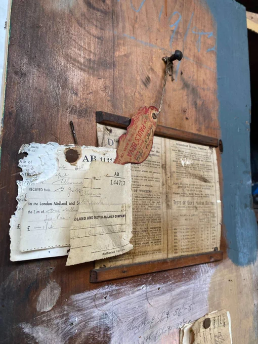 A collection of scraps of old paper, notes and receipts pinned to a wooden board. The papers are discoloured and stained, some with written notes and some typed.