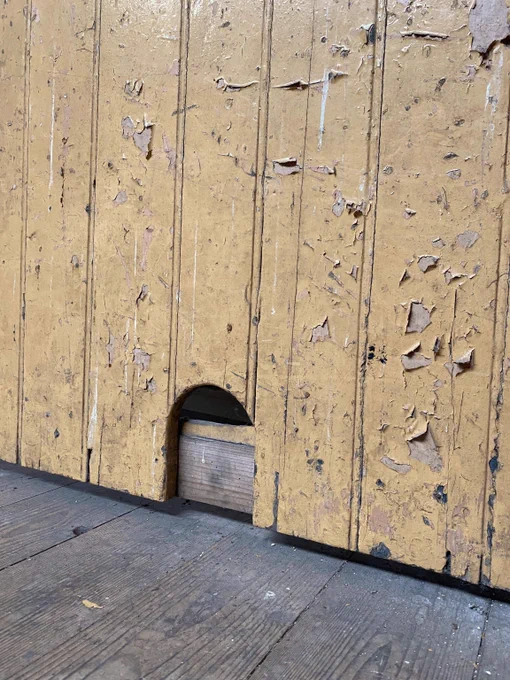 A yellow wooden door with flaking paint. At the bottom of the door is a curved hole for a cat to enter and leave the room.