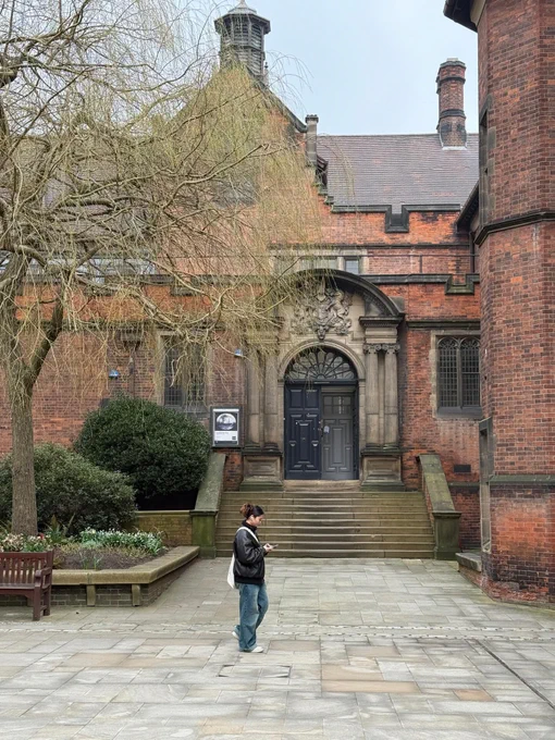A person stands in a courtyard looking towards the entrance of the traditional brick building of the Hatton Gallery, featuring a grand staircase and an archway entrance.