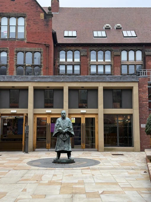 A statue of Martin Luther King Jr. stands in a courtyard in front of the brick buildings of the Newcastle University. 
