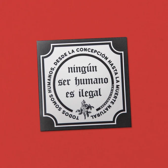 a square, black-and-white sticker sits on a red background. Text on the sticker, in Spanish, says "No human being is illegal. We are all human from conception till natural death."